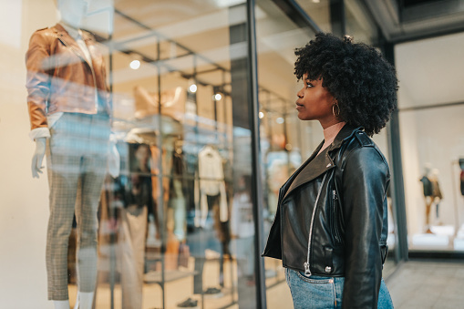 A young woman out shopping in the city. Afro female standing in front of boutique and looking in the shop window